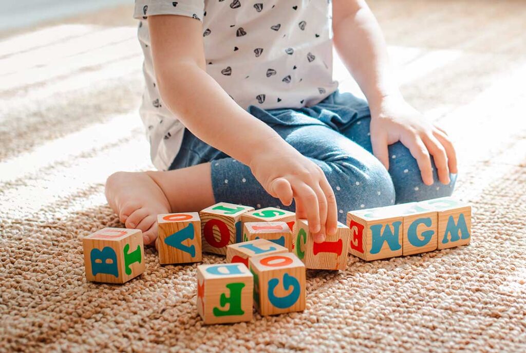Caregiver and preschool child building with blocks at a table during a play-based learning activity.