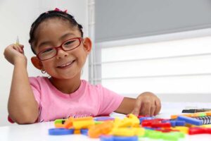 Caregiver kneels beside two young children as they share blocks and practice taking turns.